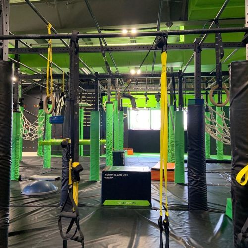 Indoor obstacle course with various climbing structures, ropes, and mats in vibrant green and black colors.
