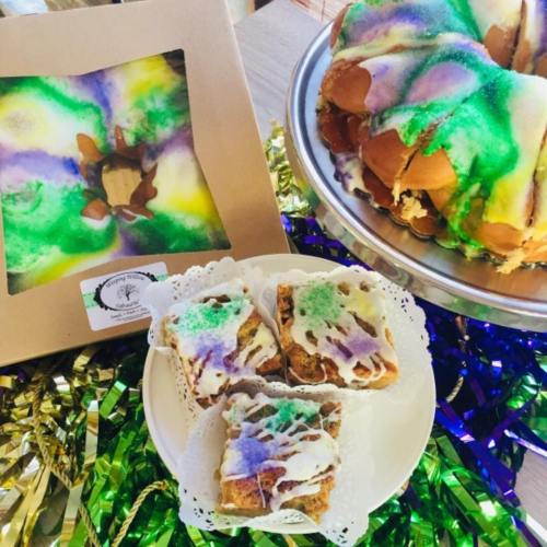 A colorful King Cake with purple, green, and gold icing, displayed with slices on a plate and a decorative box.