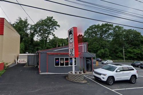 A fast-food restaurant with a red and gray exterior, featuring a large sign and parked cars in the lot.