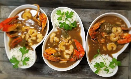 Three bowls of seafood stew with shrimp and crab, served with white rice and garnished with fresh parsley.