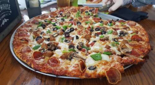 A large pizza topped with pepperoni, green peppers, olives, mushrooms, and sausage on a wooden table.