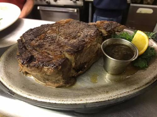 A perfectly cooked ribeye steak on a plate, garnished with a lemon wedge and a small cup of sauce.