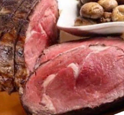A close-up of sliced roast beef with a crispy exterior, served with mushrooms on the side.