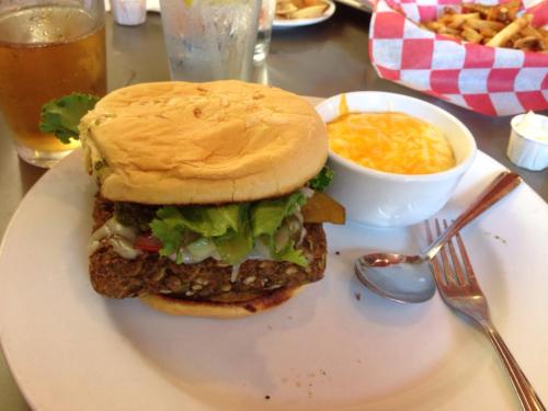 A hearty burger with lettuce and toppings, served with a side of cheese sauce and a drink in the background.