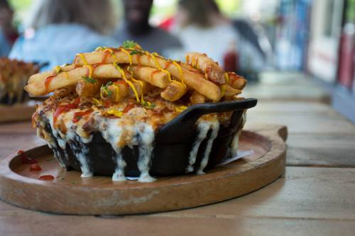 A cheesy dish topped with fries, drizzled with ketchup and mustard, served in a black skillet on a wooden table.