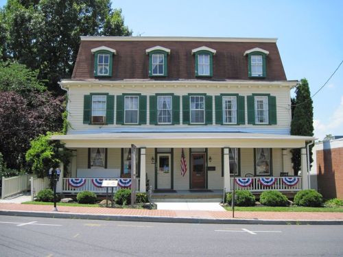 Historic building with green shutters, a brown roof, and patriotic decorations along the porch and windows.