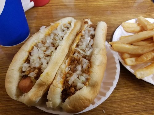 Two chili hot dogs topped with chopped onions on a paper plate, accompanied by a side of French fries.
