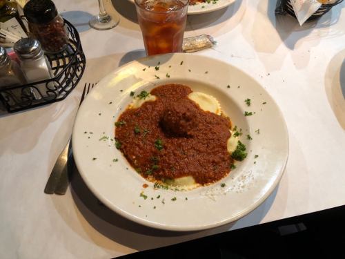 A plate of ravioli topped with meat sauce and garnished with parsley, alongside a glass of iced tea.