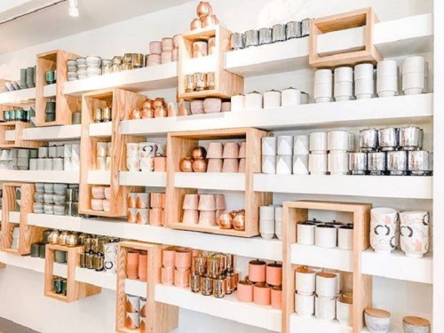 A stylish display of various candles in decorative containers arranged on wooden shelves.