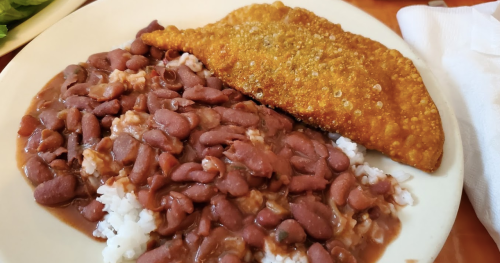 A plate of rice topped with red beans and a crispy fried fish fillet on the side.