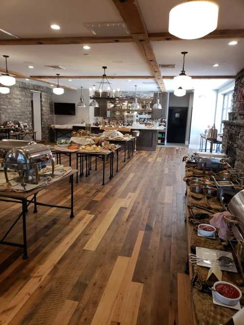 A spacious buffet setup with various food stations, wooden floors, and modern lighting in a well-lit dining area.