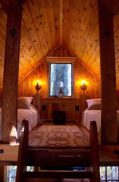 Cozy wooden cabin interior with two beds, a window, and warm lighting, featuring a rustic design and wooden beams.
