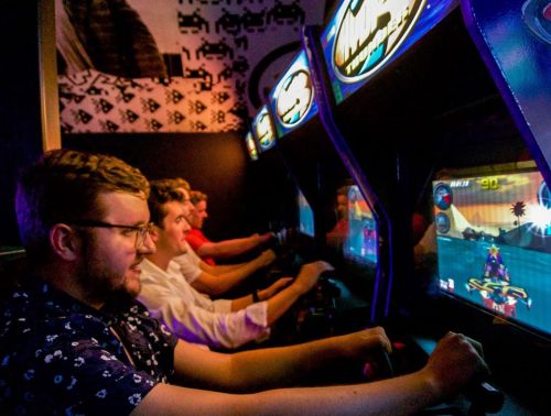 Four friends intensely playing arcade racing games, focused on the screens in a vibrant gaming environment.