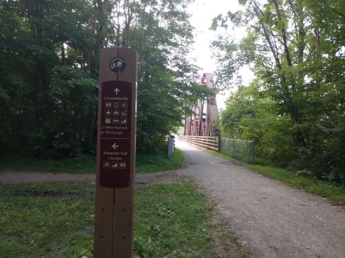 Signpost indicating directions to various locations, with a bridge visible in the background surrounded by trees.