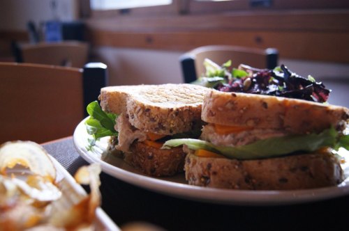 A plate with a sandwich made of whole grain bread, lettuce, cheese, and tuna, accompanied by a side salad.