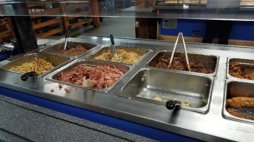 A buffet-style food station with various trays of meats, sides, and utensils for serving.