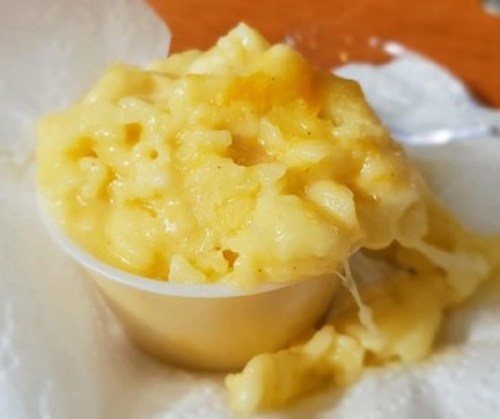 A small cup of creamy macaroni and cheese, with a gooey texture and a yellow hue, placed on a paper towel.