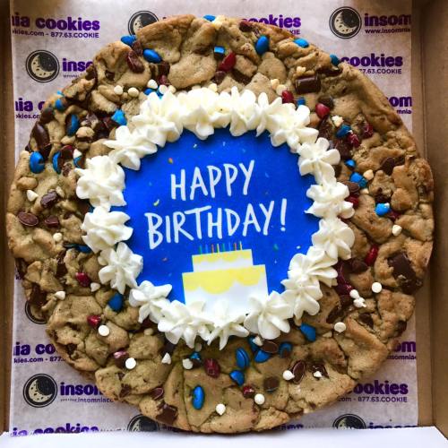 A large birthday cookie with blue icing that says "Happy Birthday!" surrounded by colorful sprinkles and chocolate chips.
