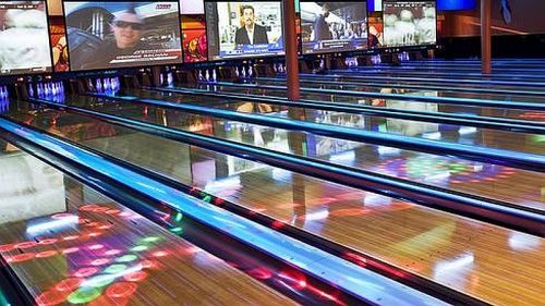 A vibrant bowling alley with illuminated lanes and screens displaying various images and news.