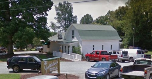 A white building with a green roof, surrounded by trees and parked cars, featuring a sign for "Yesterday's Grill."