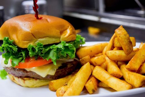 A juicy burger with lettuce, tomato, and cheese, served with a side of golden, crispy fries on a white plate.
