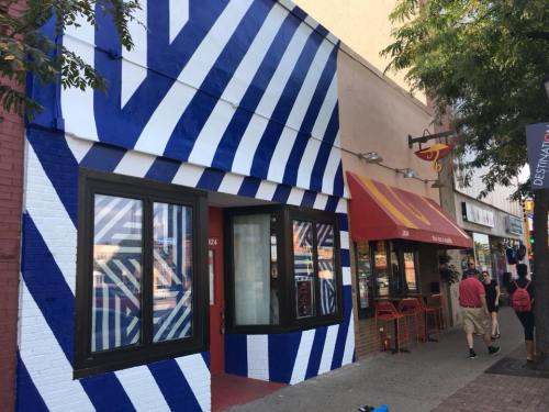 Colorful building exterior with blue and white stripes, featuring large windows and nearby shops on a busy street.
