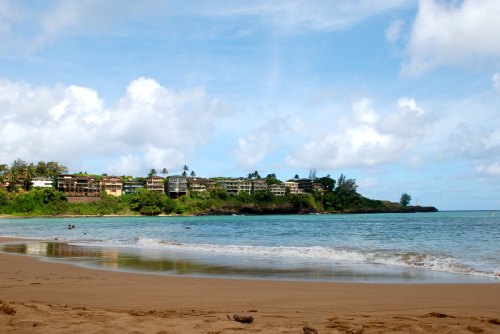 A serene beach scene with gentle waves, sandy shore, and lush greenery in the background under a partly cloudy sky.