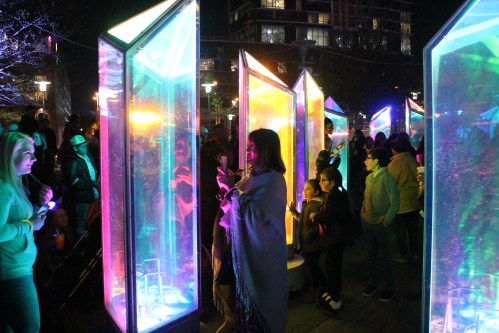 A vibrant night scene with colorful illuminated structures and people interacting in a festive atmosphere.