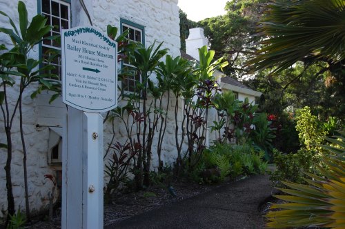 Sign for the Bailey House Museum surrounded by tropical plants and a pathway leading to the historic building.