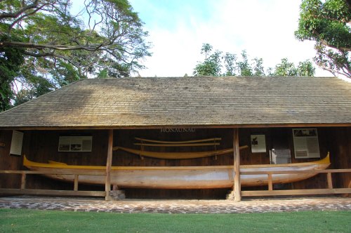 A wooden structure displays traditional canoes and paddles, surrounded by lush greenery.