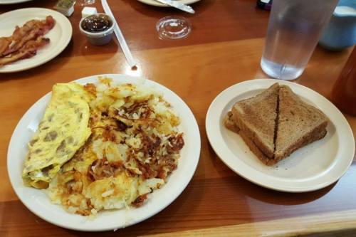 A plate with an omelet, crispy hash browns, and a side of whole grain toast, with a glass of water in the background.