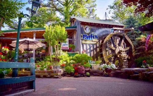 A charming restaurant with a wooden exterior, large water wheel, and vibrant flowers in a scenic outdoor setting.