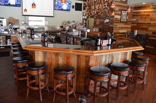 A wooden bar with high stools, surrounded by shelves of liquor, in a cozy, well-lit pub setting.