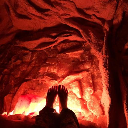 Feet resting in a warm, glowing salt cave with textured rock walls and soft red lighting.