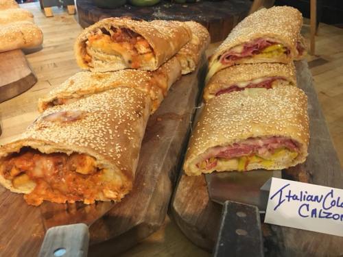 Two types of calzones on a wooden board: one with a cheesy filling and the other with ham, pickles, and cheese.