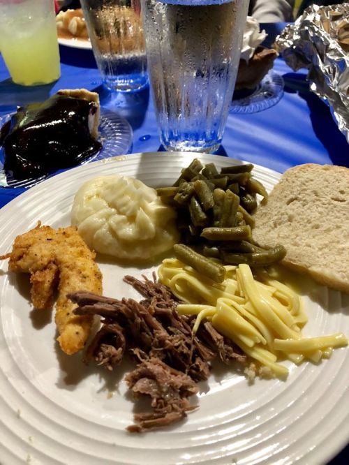 A plate of food featuring fried shrimp, mashed potatoes, green beans, pulled pork, pasta, and a slice of bread.