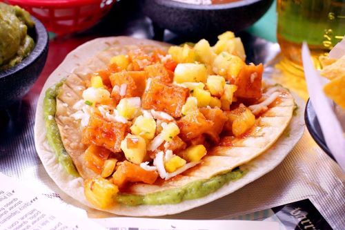 A taco topped with diced pineapple, orange squash, cheese, and green sauce, served on a tortilla.