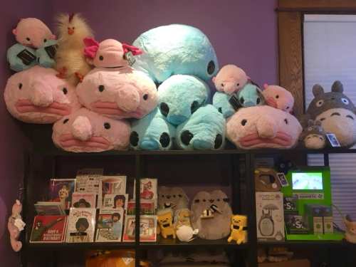 A colorful display of plush toys, including large blue and pink creatures, on a shelf with various cute merchandise.