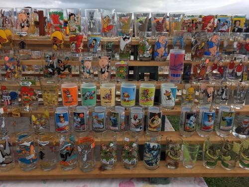 A display of colorful vintage cartoon character glasses arranged on wooden shelves at a market.