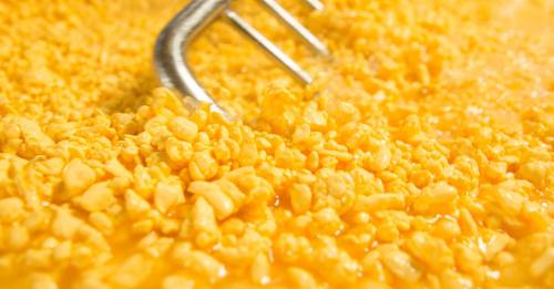 Close-up of yellow, crumbly cheese curds with a metal whisk partially submerged in the mixture.