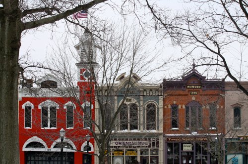 Historic buildings with varied architectural styles, framed by bare tree branches and a cloudy sky.