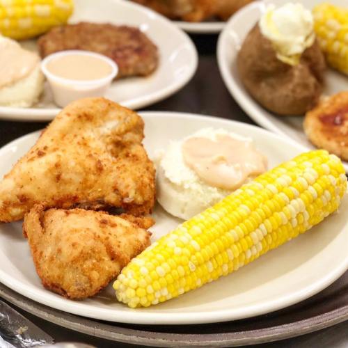A plate of fried chicken, corn on the cob, mashed potatoes with gravy, and a side of sauce.