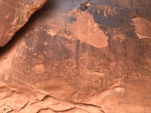 Petroglyphs etched into a rocky surface, featuring various symbols and designs in earthy tones.