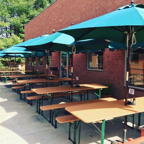 Outdoor seating area with several tables and teal umbrellas against a brick wall.