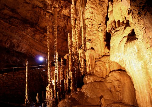 Stalactites and stalagmites in a dimly lit cave, showcasing intricate rock formations and textures.