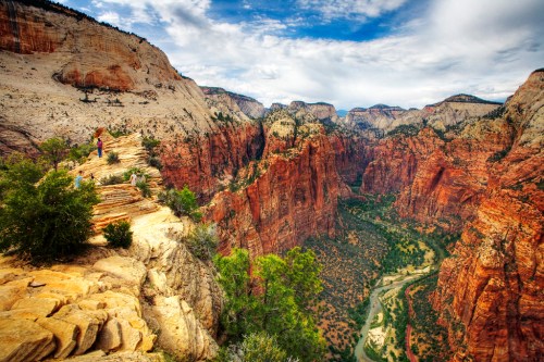 A breathtaking view of Zion National Park, showcasing red rock cliffs and a winding river below under a cloudy sky.