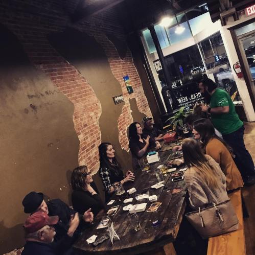 A group of people gathered around a large table in a cozy bar, enjoying drinks and conversation.