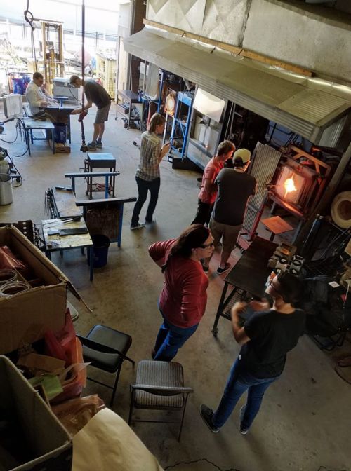 A glassblowing studio with people working on glass art, showcasing tools and equipment in a creative environment.
