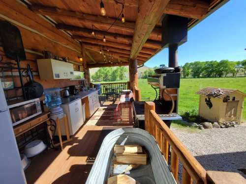 A rustic outdoor kitchen with wooden beams, appliances, and a view of green fields under a clear blue sky.