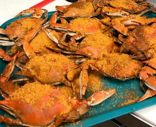 A teal tray filled with cooked crabs generously coated in a brown seasoning.